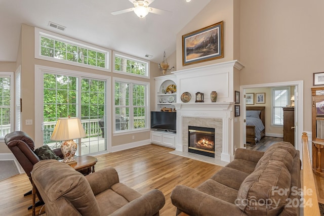 living room with light hardwood / wood-style floors, built in shelves, a premium fireplace, high vaulted ceiling, and ceiling fan