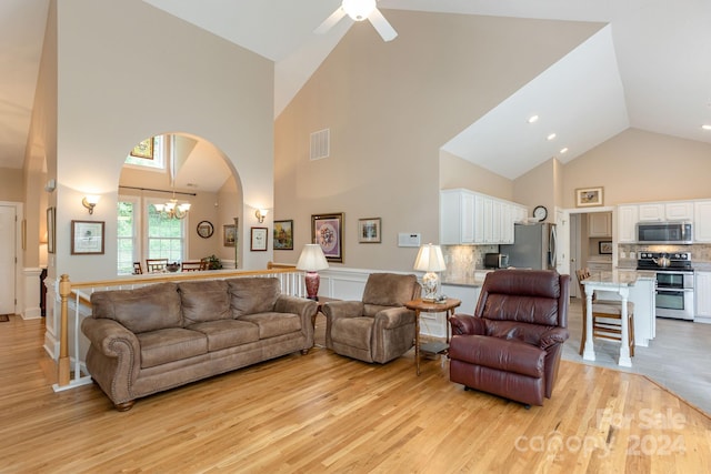 living room with high vaulted ceiling, ceiling fan with notable chandelier, and light hardwood / wood-style flooring