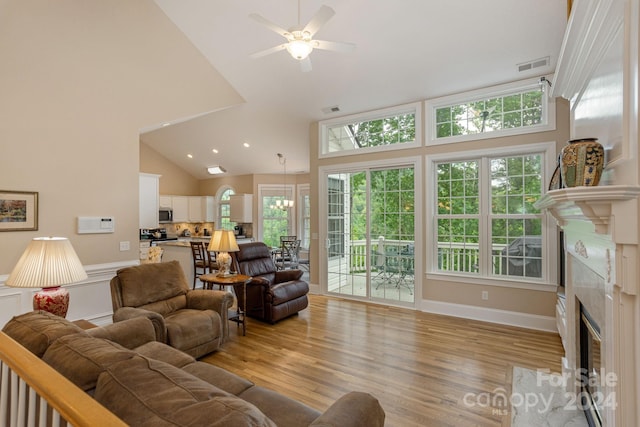 living room with a premium fireplace, ceiling fan, high vaulted ceiling, and light hardwood / wood-style flooring