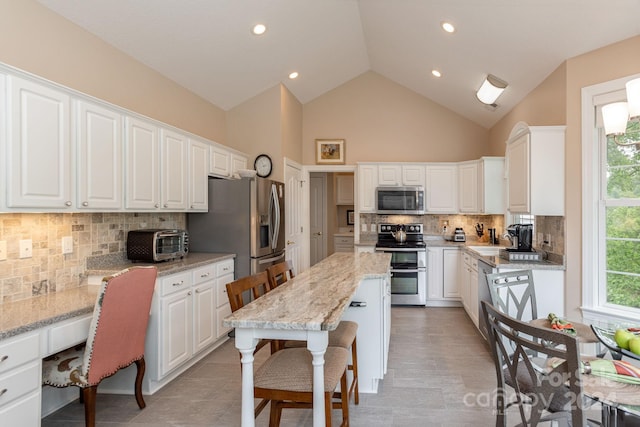 kitchen featuring light stone counters, backsplash, high vaulted ceiling, white cabinets, and appliances with stainless steel finishes