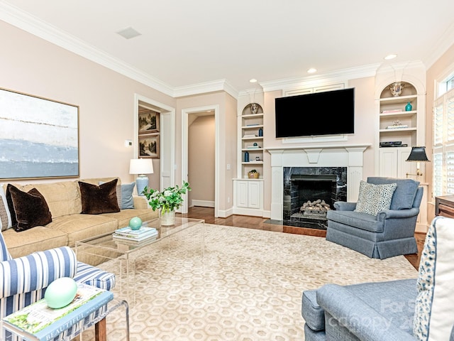 living room featuring a high end fireplace, hardwood / wood-style floors, built in features, and crown molding