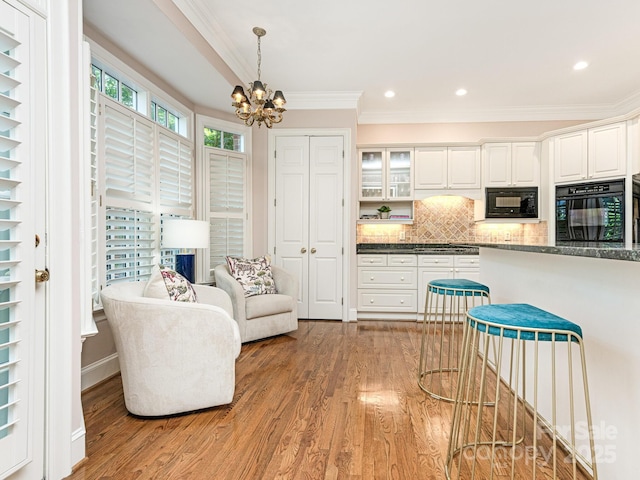 kitchen featuring backsplash, light hardwood / wood-style floors, black appliances, an inviting chandelier, and white cabinets