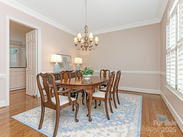 dining room with wood-type flooring, crown molding, and an inviting chandelier