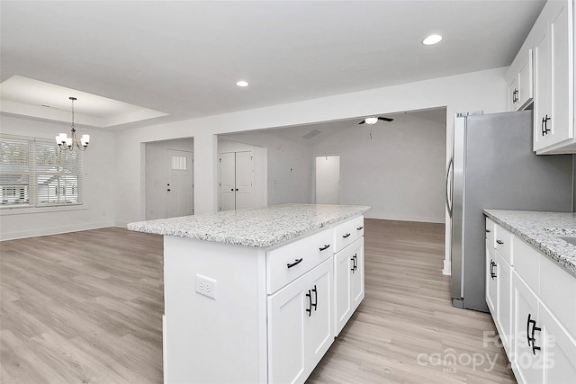 kitchen featuring white cabinetry, hanging light fixtures, a raised ceiling, a kitchen island, and light stone countertops