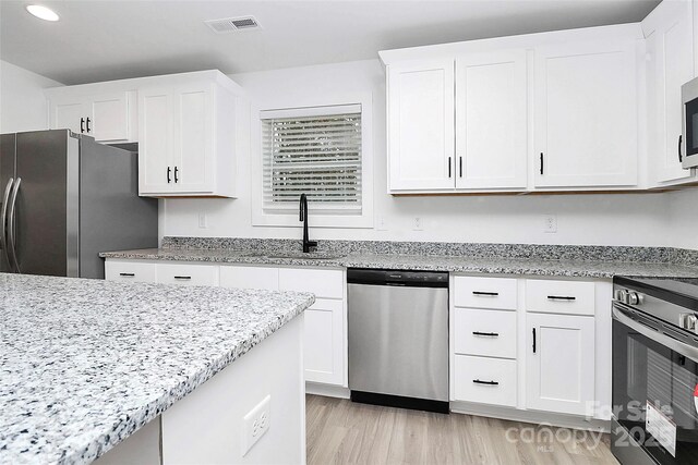 kitchen with sink, light hardwood / wood-style flooring, appliances with stainless steel finishes, light stone countertops, and white cabinets