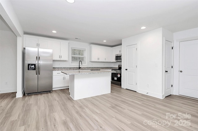 kitchen with light hardwood / wood-style flooring, appliances with stainless steel finishes, light stone counters, white cabinets, and a kitchen island