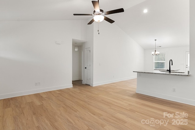 unfurnished living room with sink, ceiling fan with notable chandelier, high vaulted ceiling, and light wood-type flooring