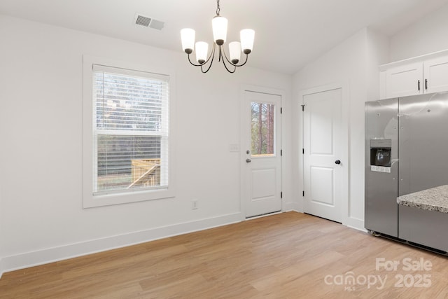 unfurnished dining area with an inviting chandelier, a healthy amount of sunlight, vaulted ceiling, and light hardwood / wood-style flooring