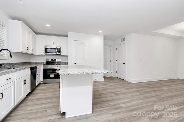 kitchen with sink, light stone counters, appliances with stainless steel finishes, a kitchen island, and white cabinets