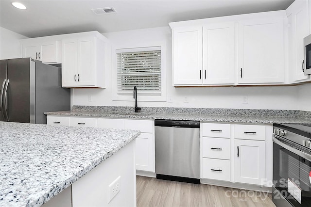 kitchen featuring sink, appliances with stainless steel finishes, light stone counters, white cabinets, and light wood-type flooring