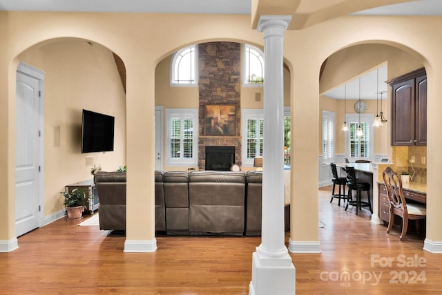 living room featuring a high ceiling, a fireplace, ornate columns, and light hardwood / wood-style flooring