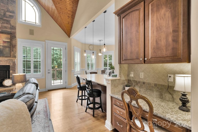 kitchen with light hardwood / wood-style floors, hanging light fixtures, a fireplace, a breakfast bar area, and backsplash