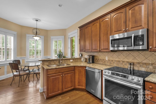 kitchen with stainless steel appliances, light stone counters, decorative light fixtures, wood-type flooring, and tasteful backsplash