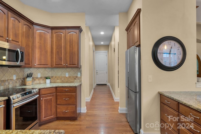 kitchen with backsplash, appliances with stainless steel finishes, hardwood / wood-style flooring, and light stone counters