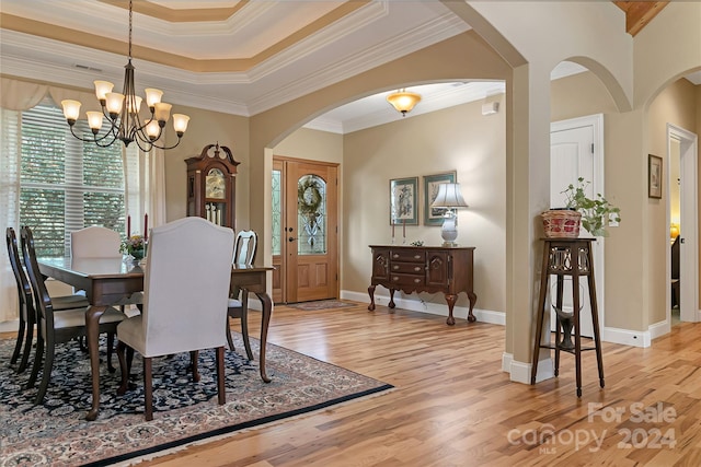 dining room featuring an inviting chandelier, light hardwood / wood-style flooring, a raised ceiling, and crown molding