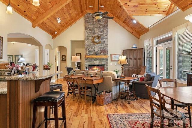 dining space with light wood-type flooring, a stone fireplace, high vaulted ceiling, wood ceiling, and ceiling fan