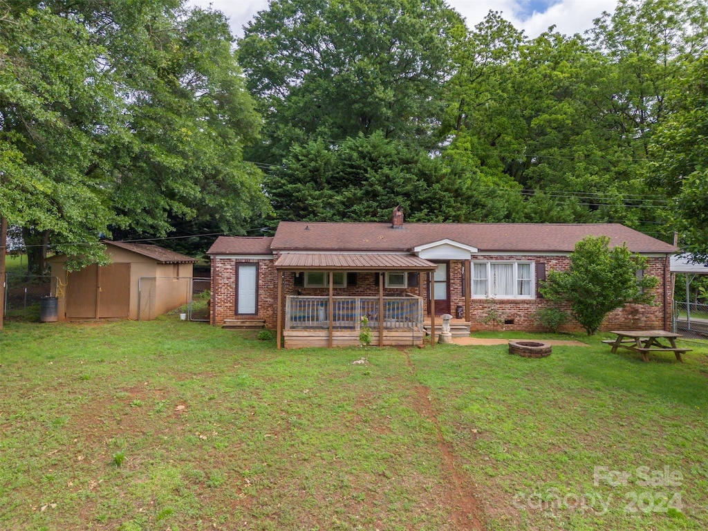 view of front of property with a wooden deck, a front yard, a fire pit, and a shed