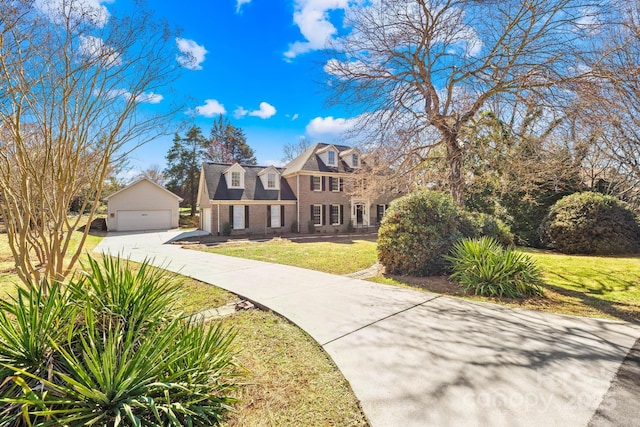 view of front of house with brick siding, a detached garage, an outdoor structure, and a front yard