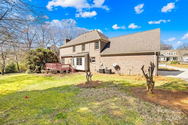 rear view of property with brick siding, a yard, a chimney, central air condition unit, and a deck