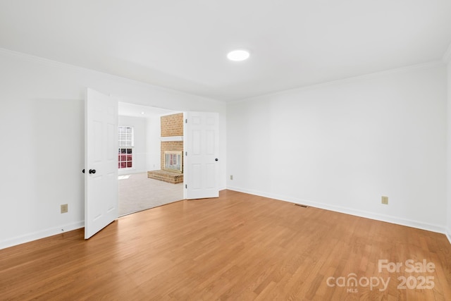 unfurnished room featuring a brick fireplace, baseboards, crown molding, and light wood finished floors