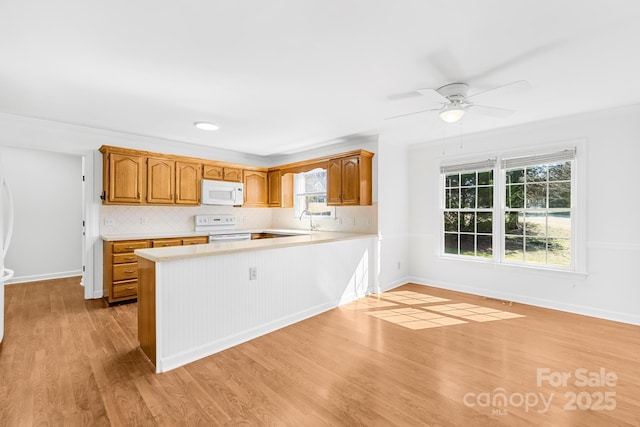 kitchen with white appliances, a peninsula, light countertops, light wood-type flooring, and backsplash