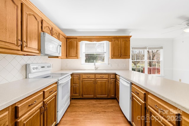 kitchen with white appliances, brown cabinetry, light wood-style flooring, light countertops, and a sink