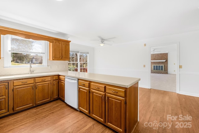 kitchen featuring light wood-style flooring, a peninsula, a fireplace, light countertops, and dishwasher