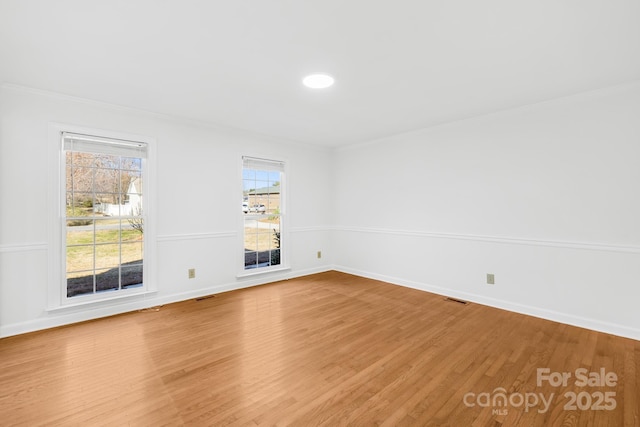 spare room with light wood finished floors, visible vents, baseboards, and crown molding