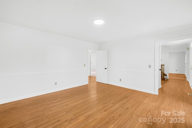 spare room with baseboards, crown molding, and light wood finished floors