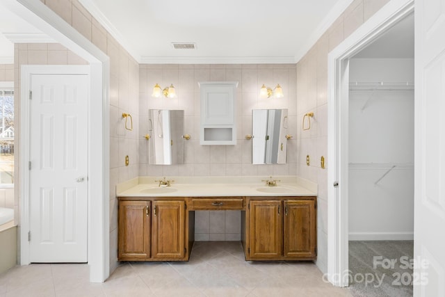 bathroom with crown molding, visible vents, a sink, and tile walls