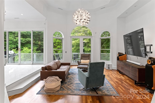 living room with wood-type flooring, a towering ceiling, crown molding, and a notable chandelier