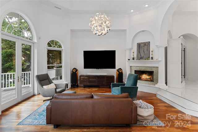 living room with french doors, a towering ceiling, crown molding, wood-type flooring, and a notable chandelier