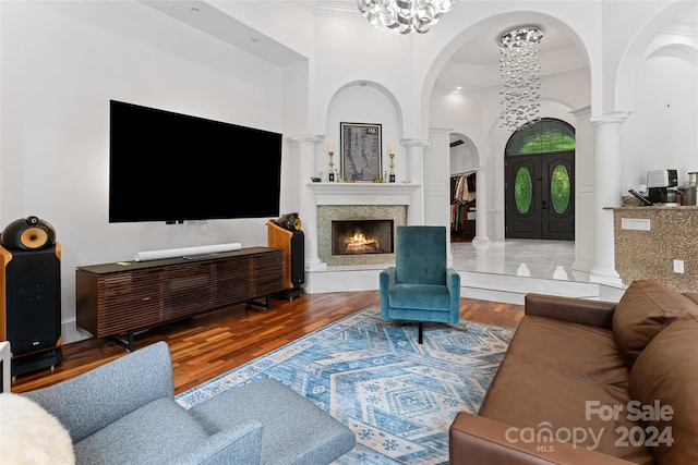 living room with a high ceiling, ornate columns, a notable chandelier, and hardwood / wood-style floors