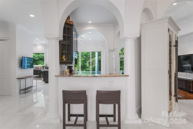 kitchen featuring kitchen peninsula, ornamental molding, light stone countertops, and a healthy amount of sunlight