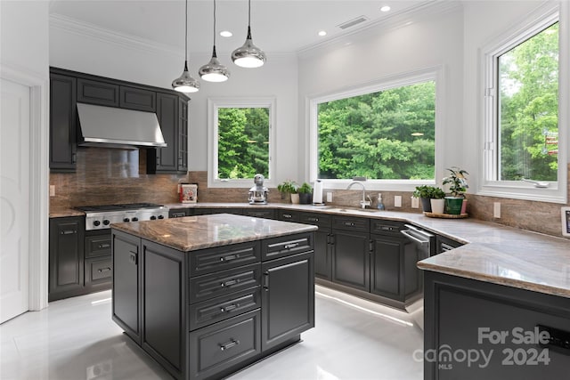 kitchen with light stone countertops, sink, a center island, hanging light fixtures, and stainless steel gas stovetop