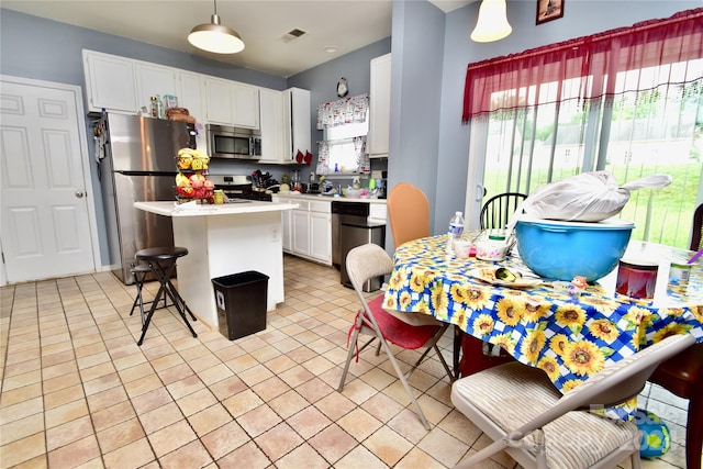 kitchen with decorative light fixtures, a kitchen island, light tile floors, white cabinets, and appliances with stainless steel finishes