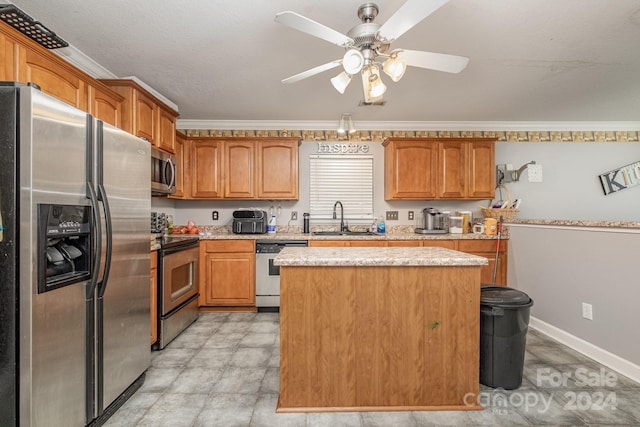 kitchen with appliances with stainless steel finishes, sink, a kitchen island, ceiling fan, and ornamental molding