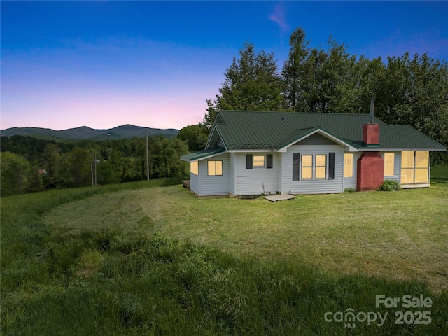 back house at dusk featuring a mountain view and a lawn