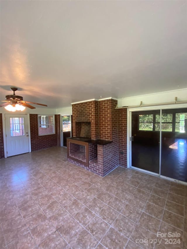 unfurnished living room with brick wall, ceiling fan, tile floors, and a fireplace