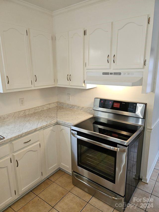 kitchen featuring white cabinetry, stainless steel electric range oven, light tile floors, and crown molding