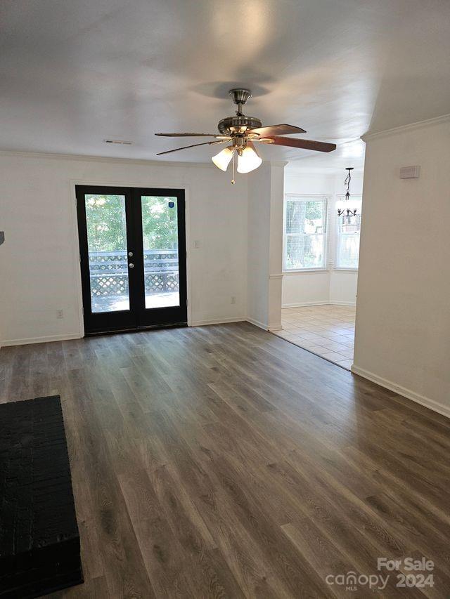 empty room with plenty of natural light, ceiling fan with notable chandelier, and dark hardwood / wood-style flooring