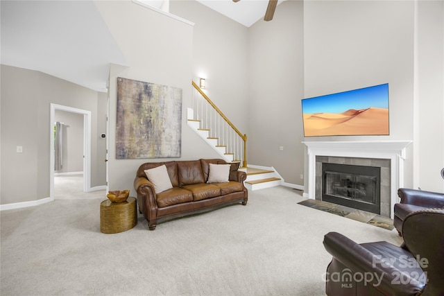 carpeted living room featuring ceiling fan, a towering ceiling, and a tiled fireplace