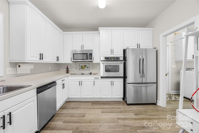 kitchen featuring washer / dryer, sink, white cabinetry, appliances with stainless steel finishes, and light hardwood / wood-style floors