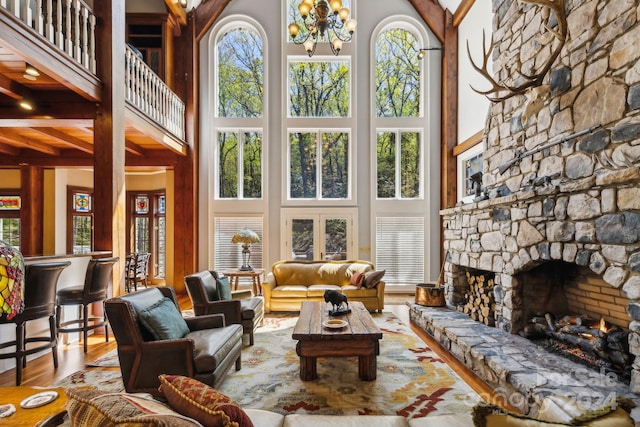 living room featuring a chandelier, a stone fireplace, beam ceiling, wood-type flooring, and a high ceiling