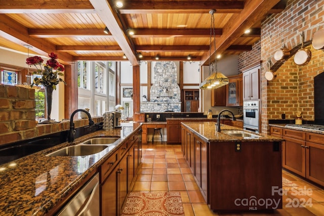 kitchen with dark stone counters, light tile flooring, a kitchen island with sink, beamed ceiling, and sink