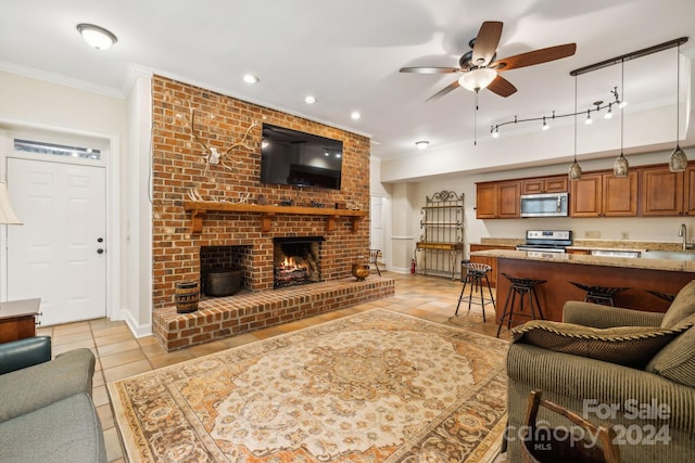 tiled living room with ceiling fan, crown molding, a brick fireplace, rail lighting, and sink