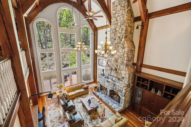 living room with a fireplace, ceiling fan with notable chandelier, beamed ceiling, hardwood / wood-style floors, and high vaulted ceiling