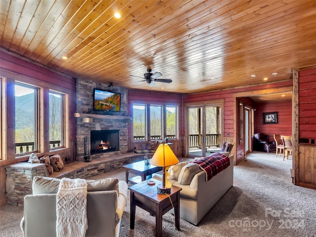 living room with a stone fireplace, ceiling fan, carpet floors, wood walls, and wooden ceiling