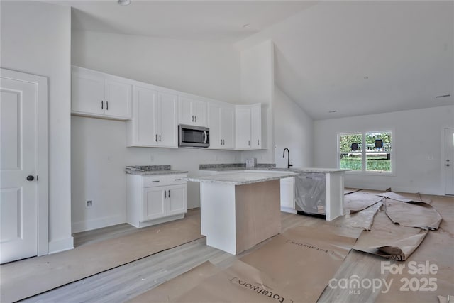 kitchen featuring white cabinets, high vaulted ceiling, and stainless steel microwave