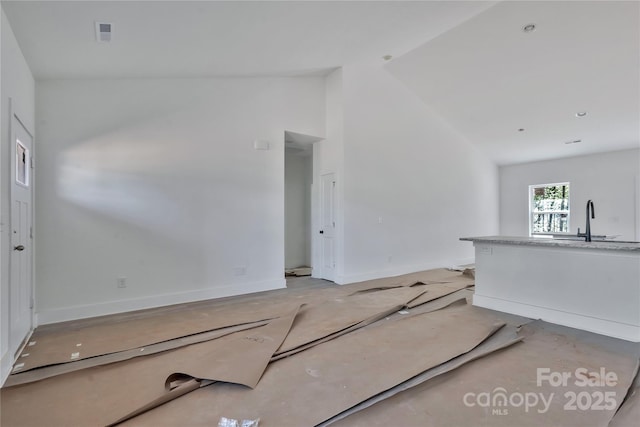 unfurnished living room with baseboards, visible vents, a sink, and high vaulted ceiling